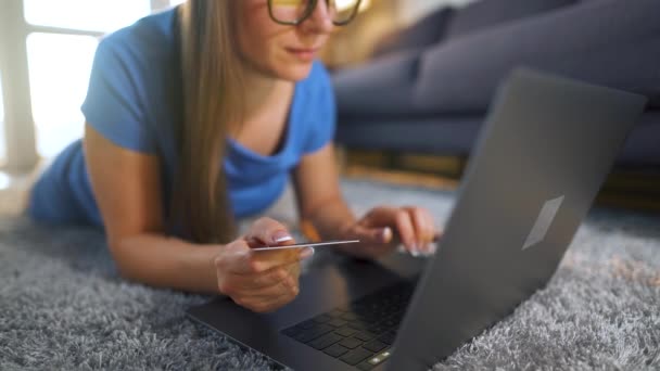 Kobieta w okularach leży na podłodze i dokonuje zakupu online za pomocą karty kredytowej i laptopa. Zakupy online, technologia stylu życia — Wideo stockowe