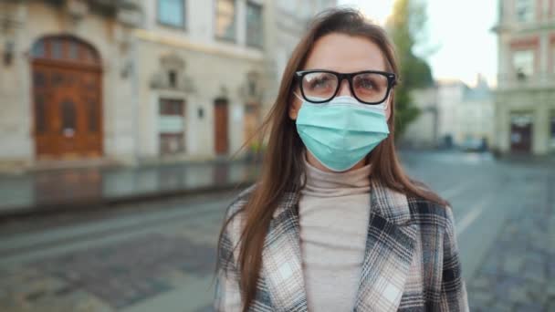 Pandemiskt skydd av Covid-19-koronavirus. Porträtt av en kvinna i rock, glasögon och en skyddande medicinsk mask. Hon står mitt på torget.. — Stockvideo