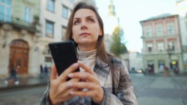 Eski bir caddede yürüyen, akıllı telefon kullanan ve fotoğraf çeken bir kadın.