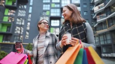 İki mutlu kadın alışveriş torbalarıyla gezer ve başarılı bir alışverişin ardından kahve alır ve kendi aralarında ilgilenerek konuşurlar..