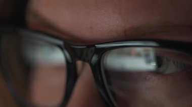 Gözlüklü kadın monitöre bakıyor ve internette sörf yapıyor. Monitör ekranı gözlüklere yansıyor. Gece çalış. İçişleri Bakanlığı. Uzak çalışma