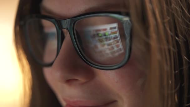Silmälasipäinen nainen katselee monitoria ja surffaa internetissä. Näytön näyttö heijastuu laseista. Yöllä töissä. Sisäministeriö. Etätyö — kuvapankkivideo