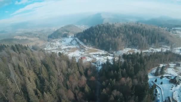 Полет над горным ландшафтом, лес на склонах, деревня у подножия горы, небольшое количество снега. — стоковое видео