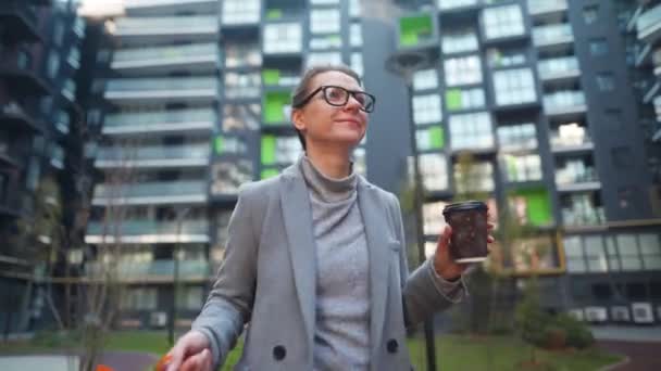 Lachende vrouw loopt in een zakenwijk met boodschappentassen en praat op de smartphone. Stedelijke levensstijl en digitale technologie — Stockvideo