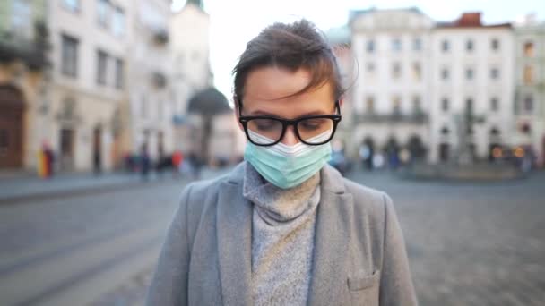 Pandemische bescherming van het Covid-19 coronavirus. Portret van een vrouw in een jas, bril en een beschermend medisch masker. Ze staat midden op het plein. Langzame beweging — Stockvideo