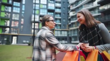 İki mutlu kadın alışveriş torbalarıyla ayakta duruyor ve kahvelerini götürüyorlar ve başarılı bir alışveriş sonrası kendi aralarında ilgilenerek konuşuyorlar..