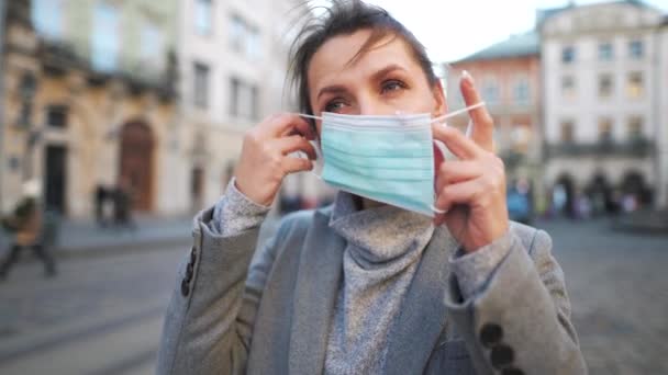 Pandemická ochrana koronaviru Covid-19. Žena v kabátě stojí uprostřed náměstí, nasazuje si ochrannou lékařskou masku — Stock video