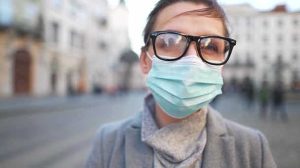 Pandemiskt skydd av Covid-19-koronavirus. Porträtt av en kvinna i rock, glasögon och en skyddande medicinsk mask. Hon står mitt på torget. Långsamma rörelser — Stockvideo