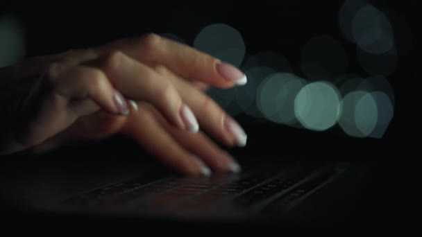 Vrouwelijke handen typen 's nachts op een laptop. wazig licht op de achtergrond — Stockvideo