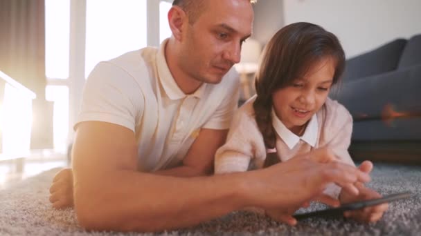 Pai e filha desfrutando de tempo juntos e usando um tablet para entretenimento familiar enquanto deitado em um chão na sala de estar em casa. — Vídeo de Stock