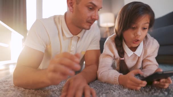 Padre e hija disfrutando del tiempo juntos y utilizando una tableta para el entretenimiento familiar mientras están acostados en el suelo en la sala de estar en casa. — Vídeo de stock