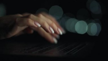 Hızlandırılmış kadın eli videosu gece bilgisayarda daktilo ediyor. Arka planda bulanık ışıklar var. Hızlı hareket. Zaman Uygulaması