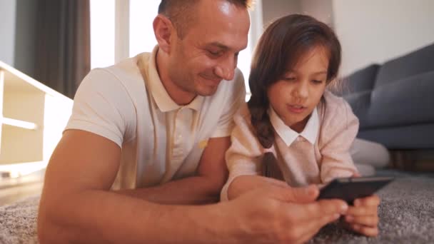 아버지와 딸 이 집 거실의 바닥에 누워 함께 시간을 즐기고 가족의 오락을 위해 태블릿을 사용하는 모습. — 비디오