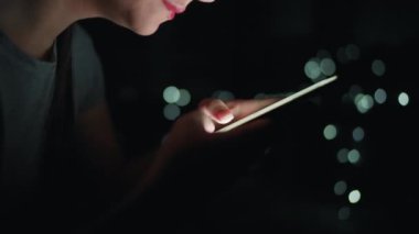 Kadın gece akıllı telefonunda daktilo kullanıyor. Arkaplanda bulanık ışıklar