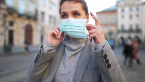 Pandemic protection of the Covid-19 coronavirus. Woman in a coat stands in the middle of the square, puts on a protective medical mask. Slow motion — Stock Video