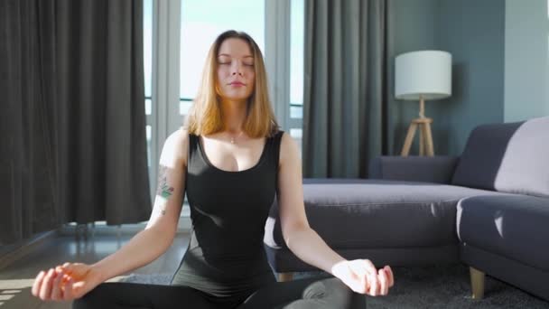 Siyah tulumlu genç beyaz kadın lotus pozisyonunda oturuyor ve meditasyon yapıyor, yoga yapıyor.. — Stok video