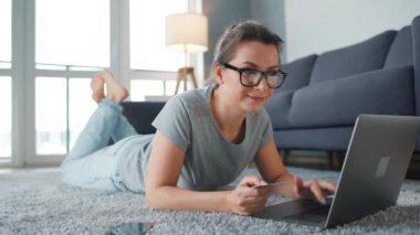 Gözlüklü kadın yerde yatıyor ve kredi kartı ve akıllı telefon kullanarak online alışveriş yapıyor. İnternetten alışveriş, yaşam tarzı teknolojisi.