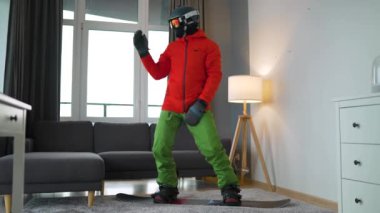 Eğlenceli video. Snowboard sporcusu gibi giyinmiş bir adam, rahat bir odada, halının üstünde dans edip eğlenirken. Karlı bir kış bekliyor. Yavaş çekim
