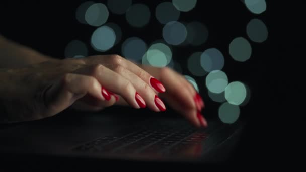 Las manos femeninas están escribiendo en un portátil por la noche. Luces borrosas en el fondo — Vídeo de stock