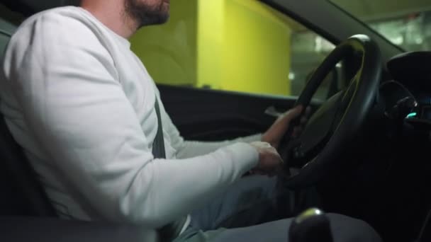 Hombre conduciendo coche a través de un estacionamiento subterráneo y está buscando un lugar para aparcar o se aleja. Vista lateral — Vídeos de Stock
