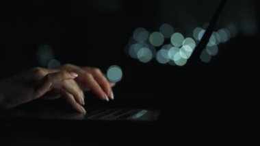 Kadın eller geceleri dizüstü bilgisayarda yazıyorlar. Gözlüğünü çıkardı ve klavyeye koydu. Arkaplanda bulanık ışıklar
