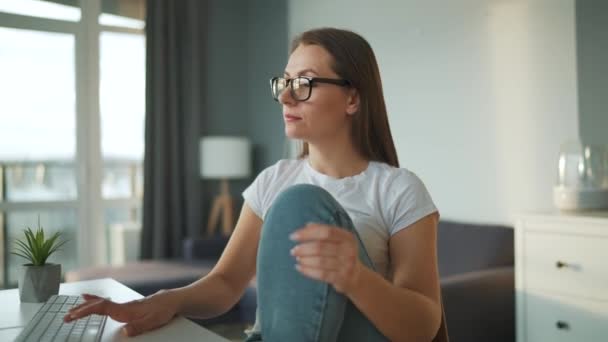 Vrijetijds geklede vrouw die thuis met een computer werkt in een gezellige omgeving. Werk op afstand buiten het kantoor. — Stockvideo