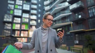 Alışveriş torbalarıyla iş bölgesinde yürüyen ve akıllı telefondan konuşan bir kadın. Kentsel yaşam tarzı ve dijital teknoloji kavramı