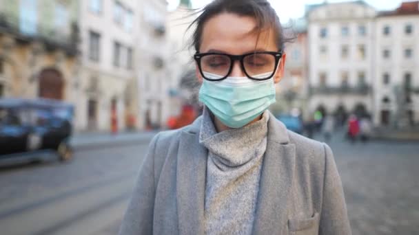 Пандемия коронавируса Ковид-19. Портрет женщины в пальто, очки и защитная медицинская маска. Она стоит посреди площади.. — стоковое видео