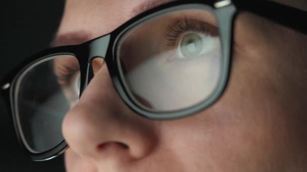 Frau mit Brille blickt auf den Monitor und arbeitet mit Diagrammen und Analysen. Der Monitor-Bildschirm spiegelt sich in der Brille wider. Arbeiten in der Nacht. Extreme Nahaufnahme — Stockvideo