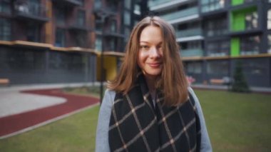 Modern binaların arka planında dikilirken büyüleyici bir şekilde gülümseyen koyu renk saçlı bir kadının portresi. Mutlu genç kadın hayattan zevk alıyor. Yavaş çekim