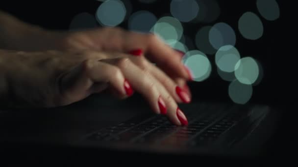 Kadın eller geceleri dizüstü bilgisayarda yazıyorlar. Arkaplanda bulanık ışıklar — Stok video