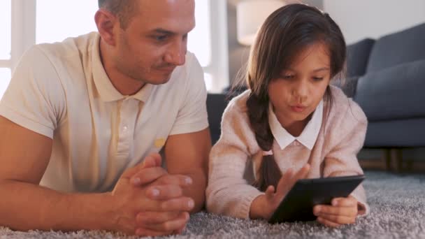 父亲和女儿一起享受时光，在家里客厅的地板上用平板电脑进行家庭娱乐. — 图库视频影像