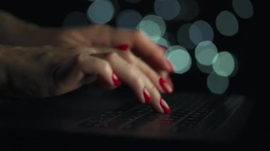 Kadın eller geceleri dizüstü bilgisayarda yazıyorlar. Arkaplanda bulanık ışıklar