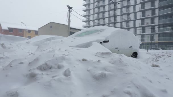 Auto 's bedekt met sneeuw na een sneeuwstorm. Woningbouw op de achtergrond. — Stockvideo