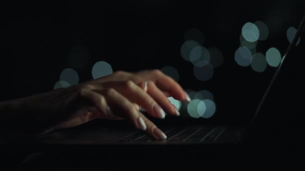 Female hands is typing on a laptop at night. She takes off and puts her glasses on the keyboard. Blurred lights on the background — Stock Video