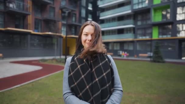 Retrato de uma linda mulher de cabelos escuros sorrindo encantadoramente enquanto está em pé contra o fundo de edifícios modernos. Jovem feliz gosta da vida. — Vídeo de Stock