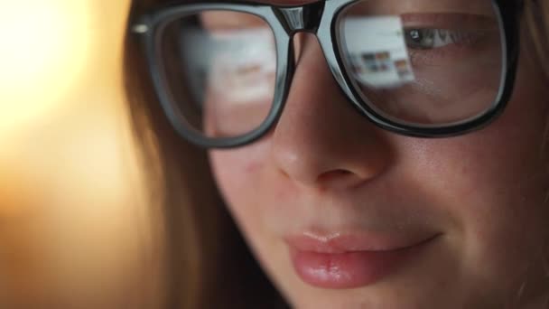 Frau mit Brille blickt auf den Monitor und surft im Internet. Der Monitor-Bildschirm spiegelt sich in der Brille wider. Arbeiten in der Nacht. Innenministerium. Fernbedienung — Stockvideo