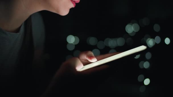 Kadın eli, gece akıllı telefonunda daktilo çalıyor. Arkaplanda bulanık ışıklar — Stok video