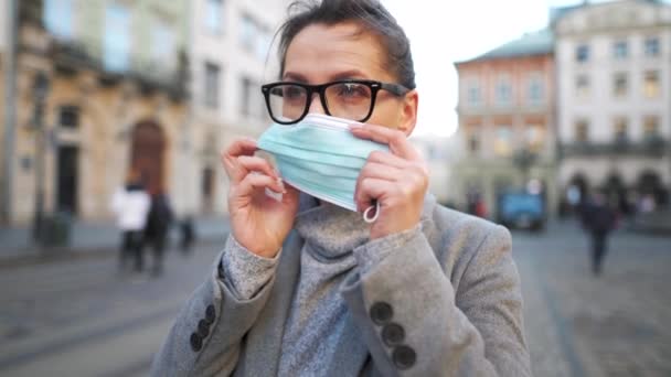 Pandemische bescherming van het Covid-19 coronavirus. Vrouw met bril staat in het midden van het plein, zet een beschermend medisch masker op. Langzame beweging — Stockvideo