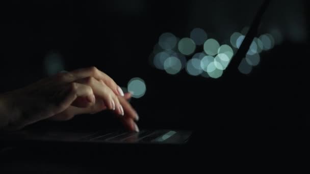 Kadın eller geceleri dizüstü bilgisayarda yazıyorlar. Gözlüğünü çıkardı ve klavyeye koydu. Arkaplanda bulanık ışıklar — Stok video