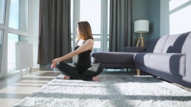 Siyah tulumlu, esnek ve dengeli olmak için evde yoga yapan beyaz bir kadın. Yavaş çekim