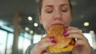 Bir kafede hamburger ve patates yiyen bir kadın. Hamburger kadınların elinde..