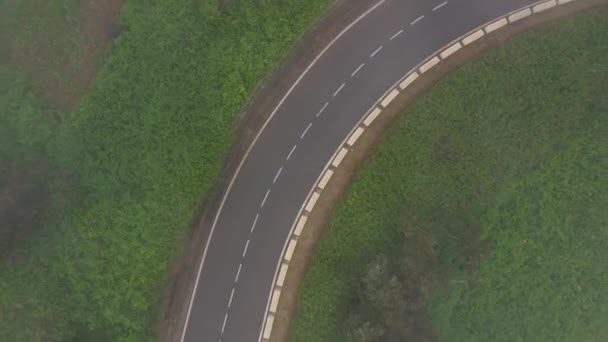 Terbang melalui awan di atas jalan pegunungan dikelilingi oleh vegetasi hijau. Mobil mengemudi di jalan. — Stok Video