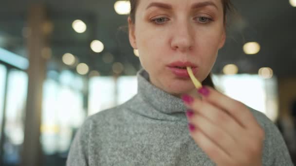 Mujer comiendo papas fritas en un café de cerca. Hamburguesa en manos femeninas. — Vídeo de stock