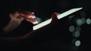 Kadın eli, gece akıllı telefonunda daktilo çalıyor. Arkaplanda bulanık ışıklar