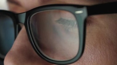 Gözlüklü kadın monitöre bakıyor ve çizelgeler ve analizlerle çalışıyor. Monitör ekranı gözlüklere yansıyor. Gece çalış. Aşırı yakın çekim