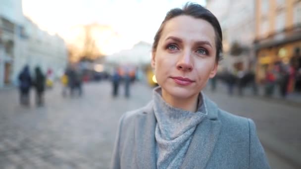 Portrait d'une femme caucasienne vêtue d'un manteau au milieu de la place de la vieille ville. Elle regarde la caméra et met des lunettes — Video