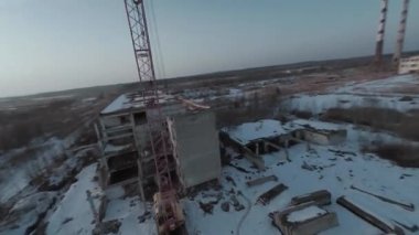 FPV insansız hava aracı, terk edilmiş sanayi binaları ve bir kazıcının etrafında hızla ve manevra kabiliyetiyle uçar..