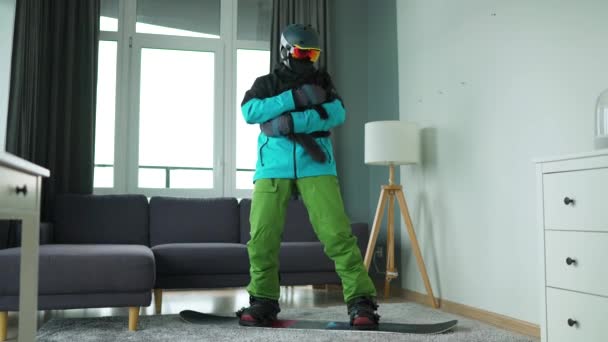 Vídeo divertido. Homem vestido como um snowboarder retrata snowboard em um tapete em uma sala aconchegante com gato fofo. À espera do início do inverno — Vídeo de Stock