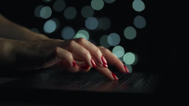 Kadın eller geceleri dizüstü bilgisayarda yazıyorlar. Gözlüklerini çıkardı ve klavyeye koydu. Arkaplanda bulanık ışıklar — Stok video
